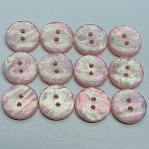 Puede incluir: Doce botones redondos rosas iridiscentes, cada uno con dos agujeros. Los botones tienen un brillo nacarado, con remolinos de rosa, blanco y sutiles toques de otros colores. Adecuados para costura y manualidades.