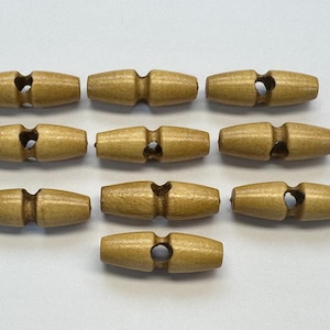 May include: Ten wooden toggle buttons are displayed. Each button is light brown, barrel-shaped, with a central hole and grooves at each end. These buttons are suitable for sewing and craft projects, and are made of wood.