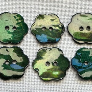 May include: A set of six flower-shaped buttons featuring a glossy, marbled finish in shades of deep forest green, emerald, and hints of light blue. Each button has a smooth, rounded edge and two central holes for attachment to fabric.