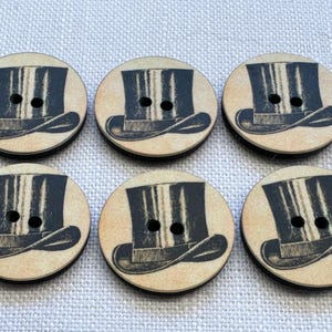 May include: Six round wooden buttons featuring a vintage top hat design. The buttons have a light brown background with a black and grey top hat illustration. Each button has two holes for sewing.