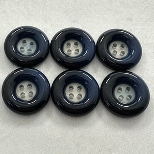 May include: Six black plastic buttons with six holes each. The buttons have a raised edge and a smooth, glossy finish.