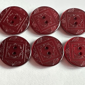 May include: Six round, dark red buttons with a square and floral design. Each button has two holes for sewing. The buttons are made of a translucent material.