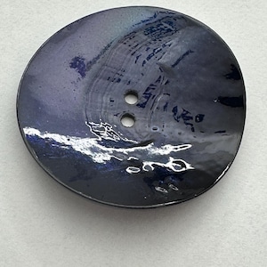 Puede incluir: Botón grande y redondo con un acabado azul oscuro iridiscente. El botón tiene dos agujeros y una superficie ligeramente texturizada. El color cambia de azul oscuro a morado y verde según la luz. Adecuado para proyectos de costura.