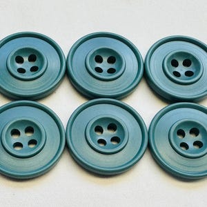 May include: Six teal-coloured, round buttons with four holes each. The buttons have a raised centre and a wide, flat outer rim. These sewing buttons are suitable for various craft and apparel projects.