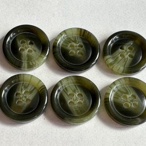 May include: Six olive green buttons with four holes each. The buttons have a marbled effect, with lighter green swirls within the darker green. The buttons are round and have a glossy finish. These buttons are suitable for sewing projects.