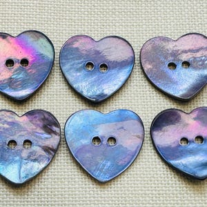 May include: Six heart-shaped buttons featuring an iridescent finish with swirling hues of deep blue, purple, and magenta. Each button has two centered holes for attachment and a smooth, reflective surface that catches light with varied color shifts.