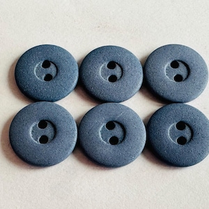 Op de afbeelding: Zes ronde, leisteenblauwe knopen met elk twee gaten zijn gerangschikt in twee rijen van drie. De knopen hebben een licht gestructureerd oppervlak en een eenvoudig, klassiek ontwerp. Deze knopen zijn geschikt voor diverse naaiprojecten.