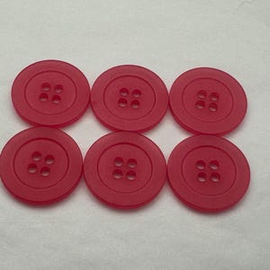 May include: Six circular, red buttons, each with four holes, are arranged in two rows of three. The buttons are a solid, vibrant red colour and appear to be plastic. They are evenly spaced against a white background.