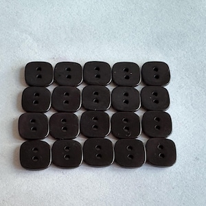 May include: A collection of twenty dark brown, square buttons with two holes each. The buttons are arranged in a grid pattern on a light gray surface. These buttons are suitable for sewing and craft projects.
