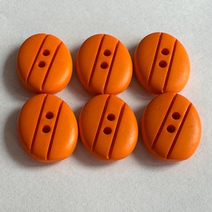 May include: Six bright orange oval buttons, each with two holes and diagonal grooves. These buttons are a solid colour and suitable for sewing and craft projects. The buttons are arranged in two rows of three.