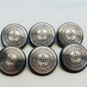 以下が含まれることがあります： コンパスのようなパターンと複雑なディテールが特徴の円形デザインの銀色のボタンが6つ。ボタンは黒い縁取りがされています。