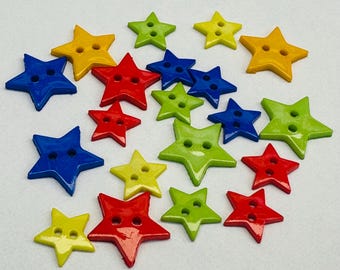 May include: A collection of star-shaped buttons in various colors, including yellow, red, blue, and green. Each button has two holes for sewing. The buttons are scattered on a white surface.