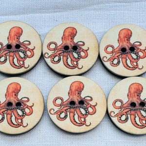 Puede incluir: Seis botones redondos de madera con diseño de pulpo. Cada botón presenta un fondo beige claro con una ilustración detallada de un pulpo rojo. El pulpo tiene ojos negros y está centrado en el botón.