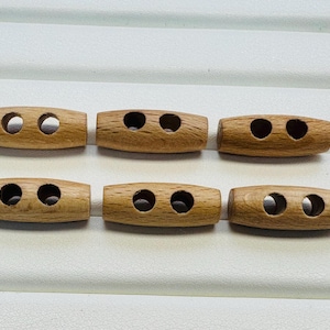 以下が含まれることがあります： 2つの穴がある6つの木製のトグルボタン。ボタンは明るい茶色で、滑らかで丸みを帯びた形をしています。これらのボタンは、コート、セーター、またはその他の衣服に最適です。