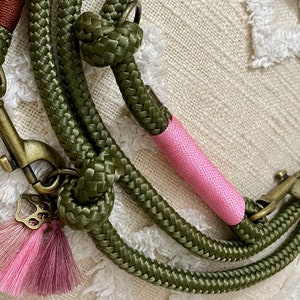 May include: A green rope dog leash with a pink accent and a gold metal clasp. The leash has a pink tassel with a gold butterfly charm.