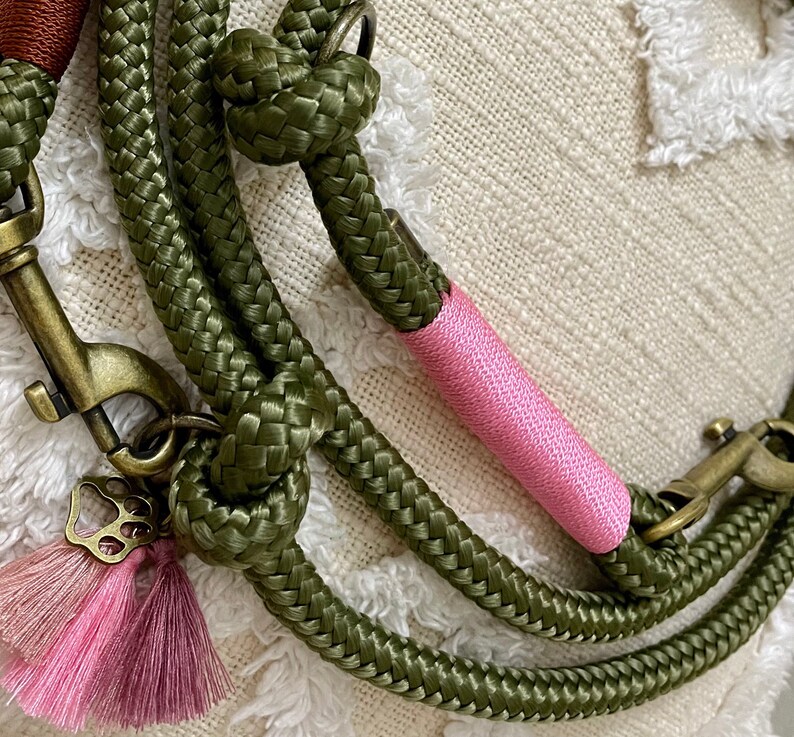 May include: A green rope dog leash with a pink accent and a gold metal clasp. The leash has a pink tassel with a gold butterfly charm.