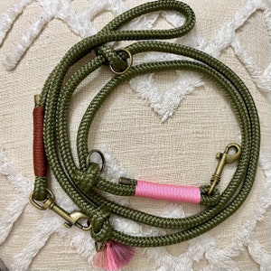 May include: A green rope dog leash with a pink accent and a brass clasp. The leash has a brown accent and a tassel.