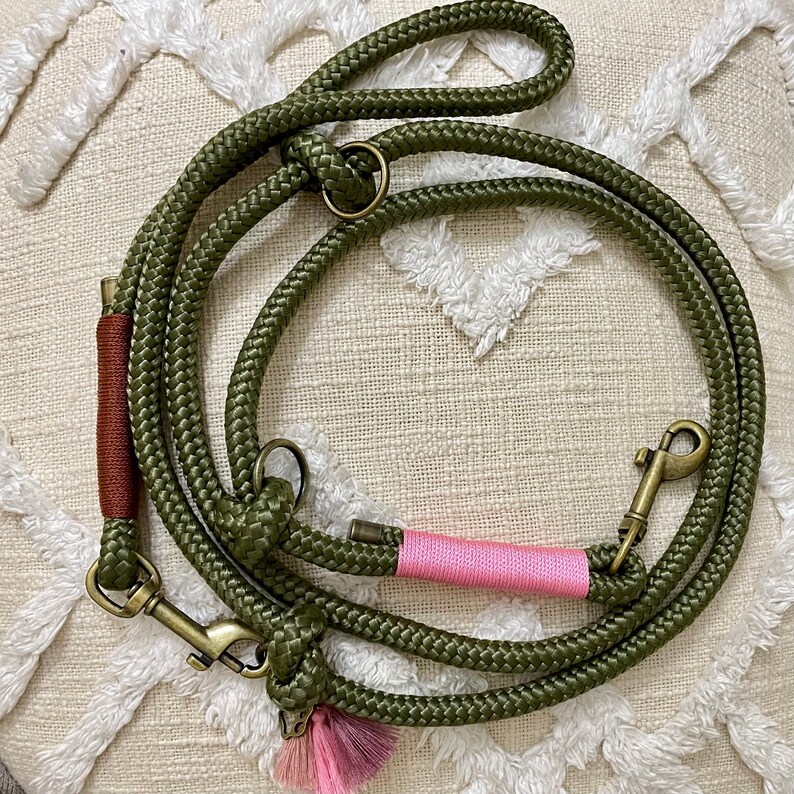May include: A green rope dog leash with a pink accent and a brass clasp. The leash has a brown accent and a tassel.