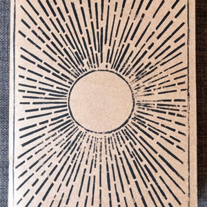 Peut inclure: Une carte en papier brun avec un motif de soleil noir. Le soleil est composé d'un cercle avec des lignes qui en rayonnent.
