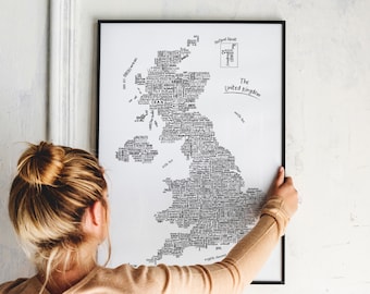 May include: A black and white print of a map of the United Kingdom. The map is made up of words that represent different places in the UK. The words are arranged in the shape of the UK. The print is framed in a black frame and is hanging on a white wall.