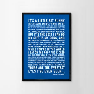 May include: A blue and black framed print with white text. The text is the lyrics to the song "Your Song" by Elton John. The lyrics include the lines "It's a little bit funny this feeling inside I'm not one of those who can easily hide I don't have much money, but..." and "Yours are the sweetest eyes I've ever seen..."