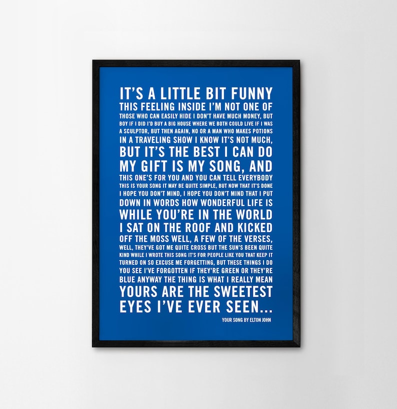 May include: A blue and black framed print with white text. The text is the lyrics to the song "Your Song" by Elton John. The lyrics include the lines "It's a little bit funny this feeling inside I'm not one of those who can easily hide I don't have much money, but..." and "Yours are the sweetest eyes I've ever seen..."