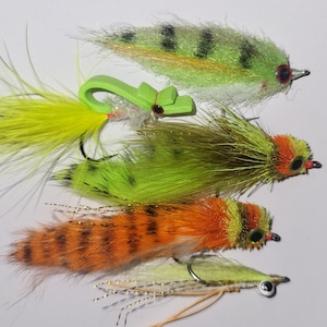 May include: A collection of colorful fishing lures. The lures feature various designs, including green, orange, and yellow feathers, with black and red accents. Each lure has a hook and is designed for catching fish.