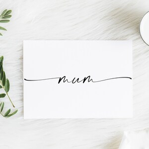 May include: A white card with the word "mum" written in black cursive script on a white background.