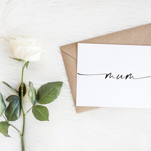 May include: A white card with the word "mum" written in cursive on it. The card is sitting on a brown envelope. A single white rose with green leaves is on the left side of the image.