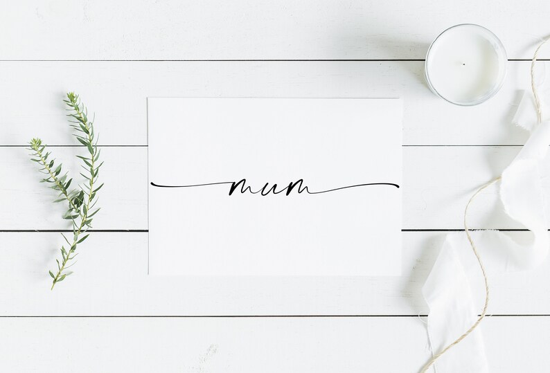 May include: A white card with the word "mum" written in black cursive script on a white wooden background. There is a small white candle and a piece of white fabric with twine on the right side of the image.