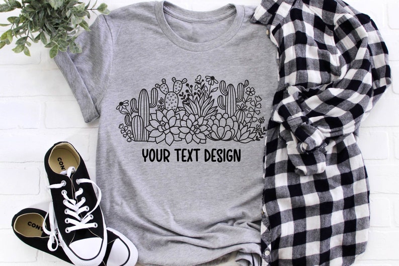 May include: A gray t-shirt with a black and white graphic of a cactus and succulent garden. The text "YOUR TEXT DESIGN" is printed below the graphic.