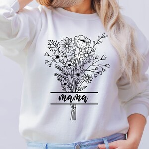 May include: White sweatshirt featuring a black floral bouquet design with the word "mama" in a banner. The bouquet includes various flower types and foliage, creating a delicate and detailed illustration. The design is centered on the front of the sweatshirt.