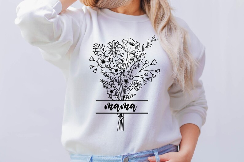 May include: White sweatshirt featuring a black floral bouquet design with the word "mama" in a banner. The bouquet includes various flower types and foliage, creating a delicate and detailed illustration. The design is centered on the front of the sweatshirt.