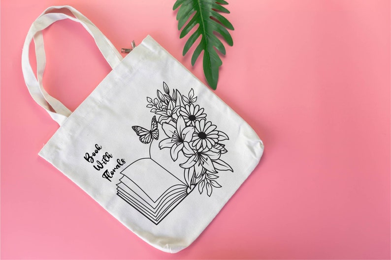 May include: White canvas tote bag with black text that reads "Book With Florals" and a black line drawing of an open book with flowers and a butterfly.