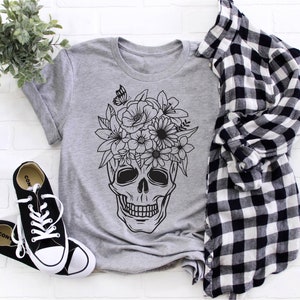 May include: A gray t-shirt with a black and white graphic of a skull with flowers on top. The skull has a floral crown with a butterfly.
