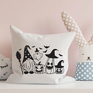 May include: A white pillow with a black and white Halloween-themed design featuring a gnome, a ghost, and pumpkins. The design includes bats and stars.