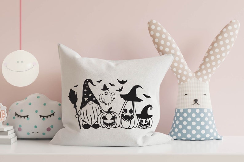 May include: A white pillow with a black and white Halloween-themed design featuring a gnome, a ghost, and pumpkins. The design includes bats and stars.