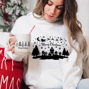 May include: White hoodie with a black and white Christmas design featuring a silhouette of a town, trees, Santa Claus in a sleigh, and the text "Merry Christmas".