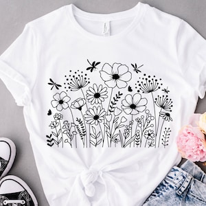 K&ouml;nnte beinhalten: Wei&szlig;es T-Shirt mit einer schwarzen Linienzeichnung eines Blumenstrau&szlig;es und Libellen.