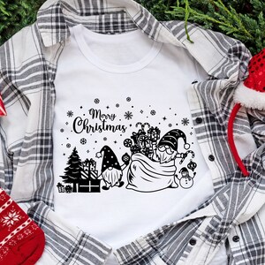May include: White t-shirt with a black and white design of two gnomes carrying a bag of presents. The design also includes a Christmas tree, snowflakes, and the text "Merry Christmas".
