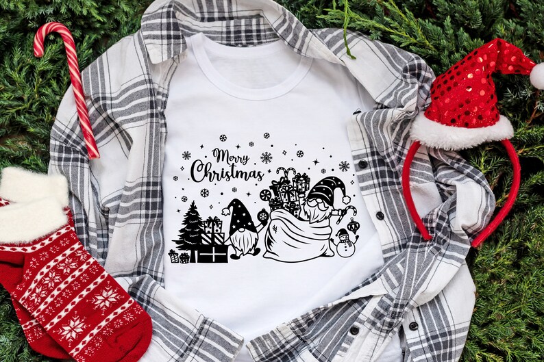 May include: White t-shirt with a black and white design of two gnomes carrying a bag of presents. The design also includes a Christmas tree, snowflakes, and the text "Merry Christmas".