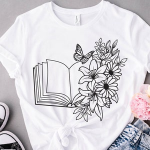 May include: White t-shirt with a black line drawing of an open book with flowers and a butterfly.