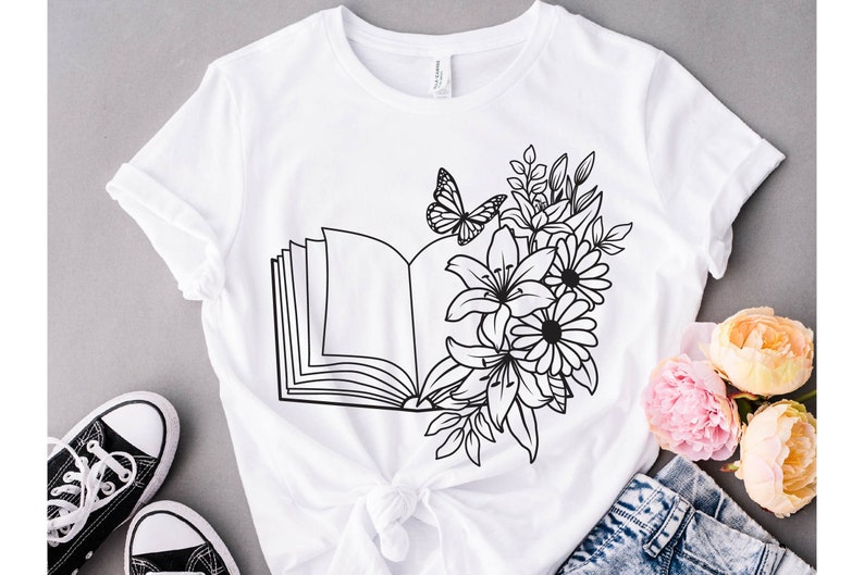 May include: White t-shirt with a black line drawing of an open book with flowers and a butterfly.