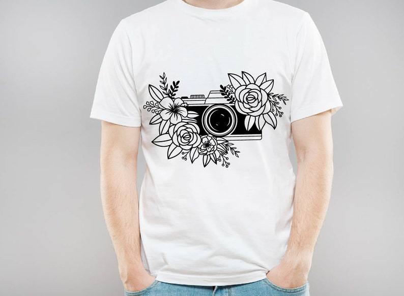 K&ouml;nnte beinhalten: Ein wei&szlig;es T-Shirt mit einer schwarz-wei&szlig;en Illustration einer Kamera, die von Blumen umgeben ist.