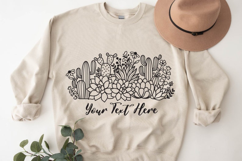 May include: A beige sweatshirt with a black and white graphic of cacti and succulents. The text "Your Text Here" is printed below the graphic.