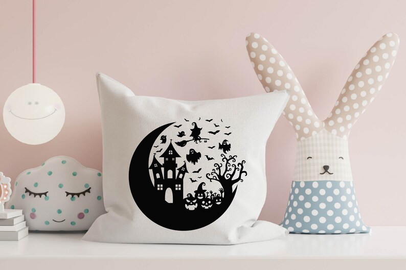 May include: White pillow with a black silhouette of a crescent moon, a haunted house, a witch flying on a broomstick, a tree, and pumpkins. The design is perfect for Halloween.