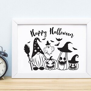 May include: A white framed print with the text "Happy Halloween" in black script. The print features a black and white illustration of a gnome wearing a pointed hat with stars, holding a broom, and standing next to a ghost, a pumpkin, and two jack-o'-lanterns.