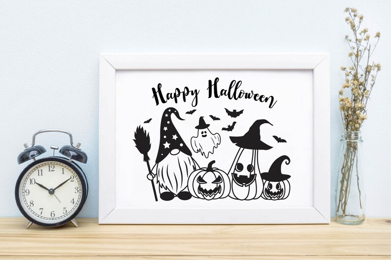 May include: A white framed print with the text "Happy Halloween" in black script. The print features a black and white illustration of a gnome wearing a pointed hat with stars, holding a broom, and standing next to a ghost, a pumpkin, and two jack-o'-lanterns.