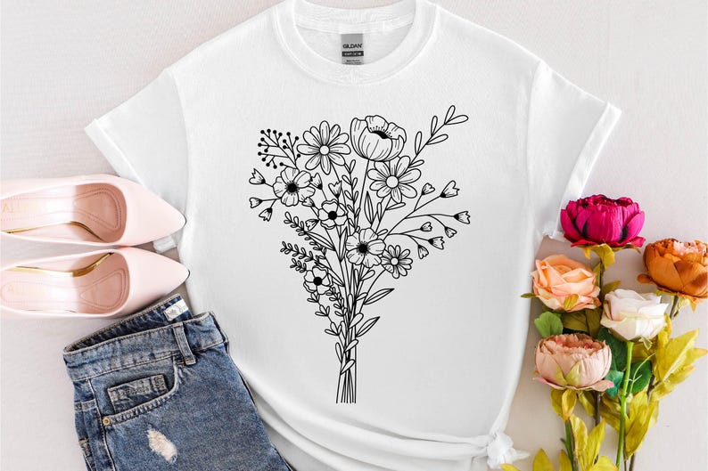 May include: White t-shirt featuring a black line drawing of a floral bouquet. The design includes various flowers and leaves tied together. The image also shows pink heels and blue jeans.