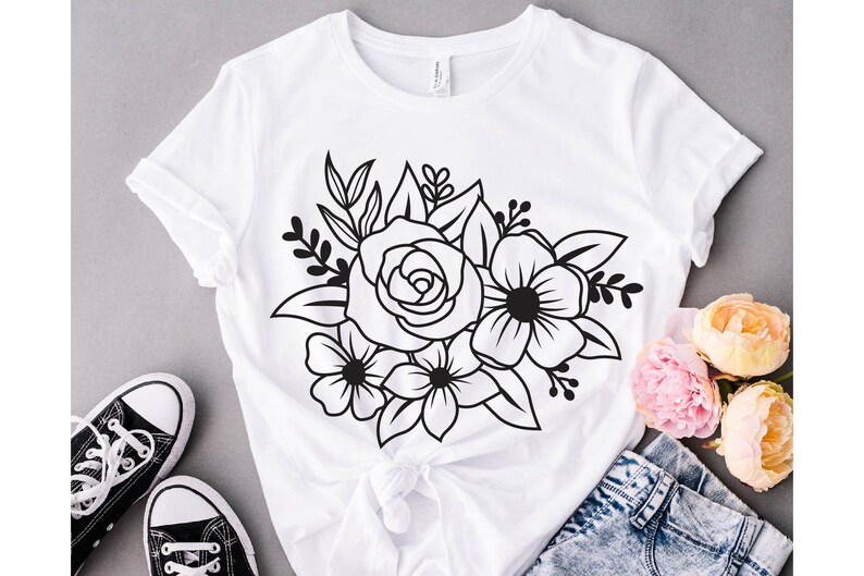 May include: A white t-shirt with a black floral design featuring a large rose and smaller flowers. The design is centered on the shirt and is surrounded by leaves.